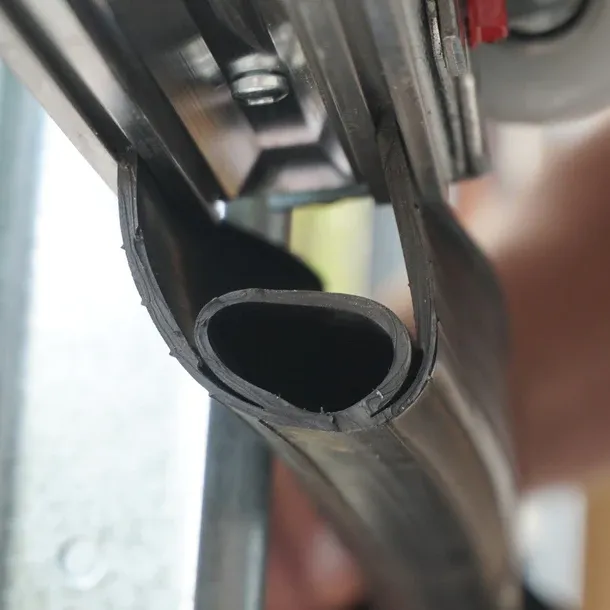 Close view of a hollow bulb rubber bottom seal being fitted into the retainer on a garage door bottom rail
