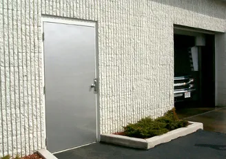 Stainless entry door installed in a masonry car wash wall beside an open overhead door bay