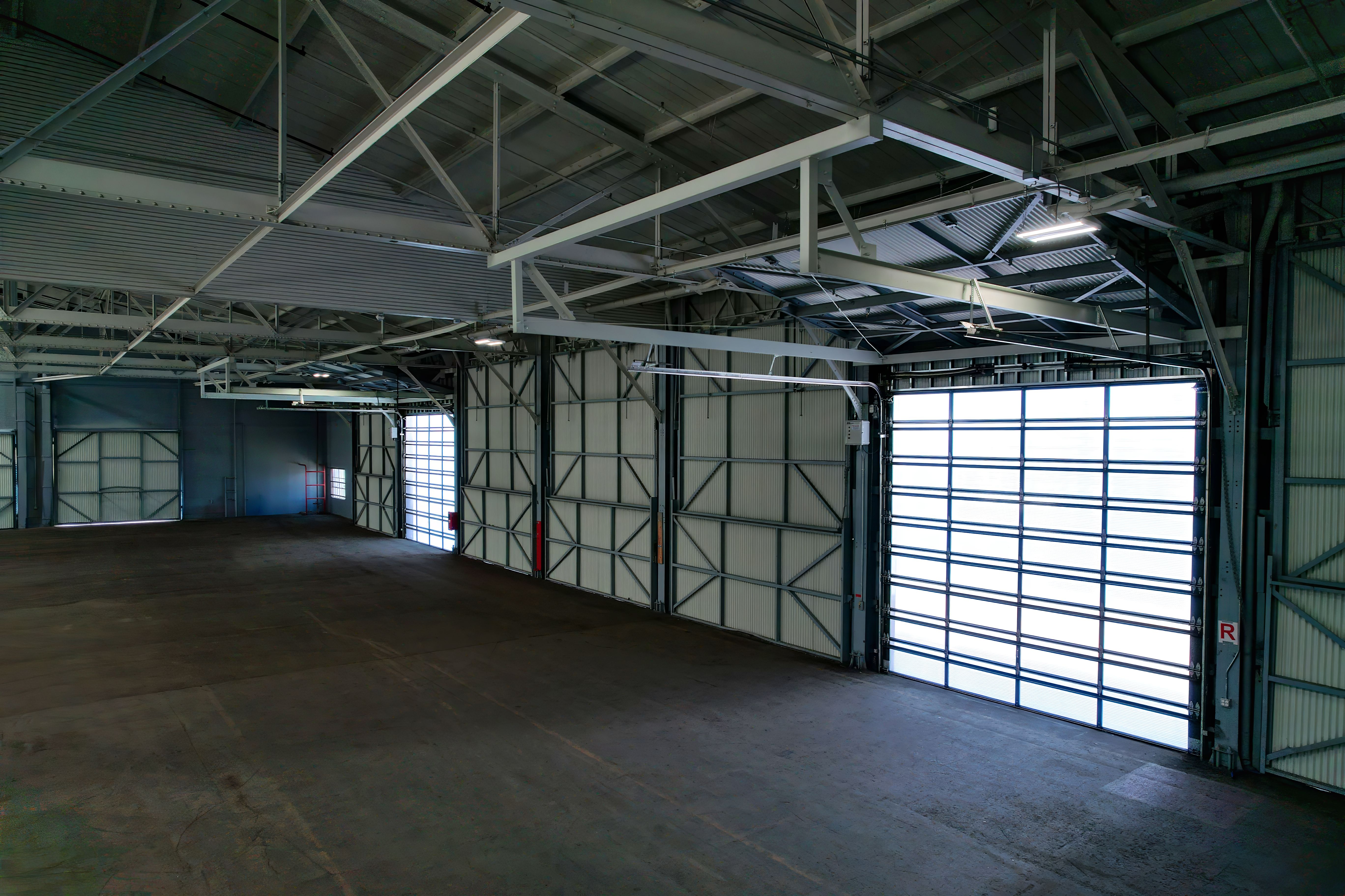 Wide interior of an empty concrete bay with two closed translucent doors glowing along the wall
