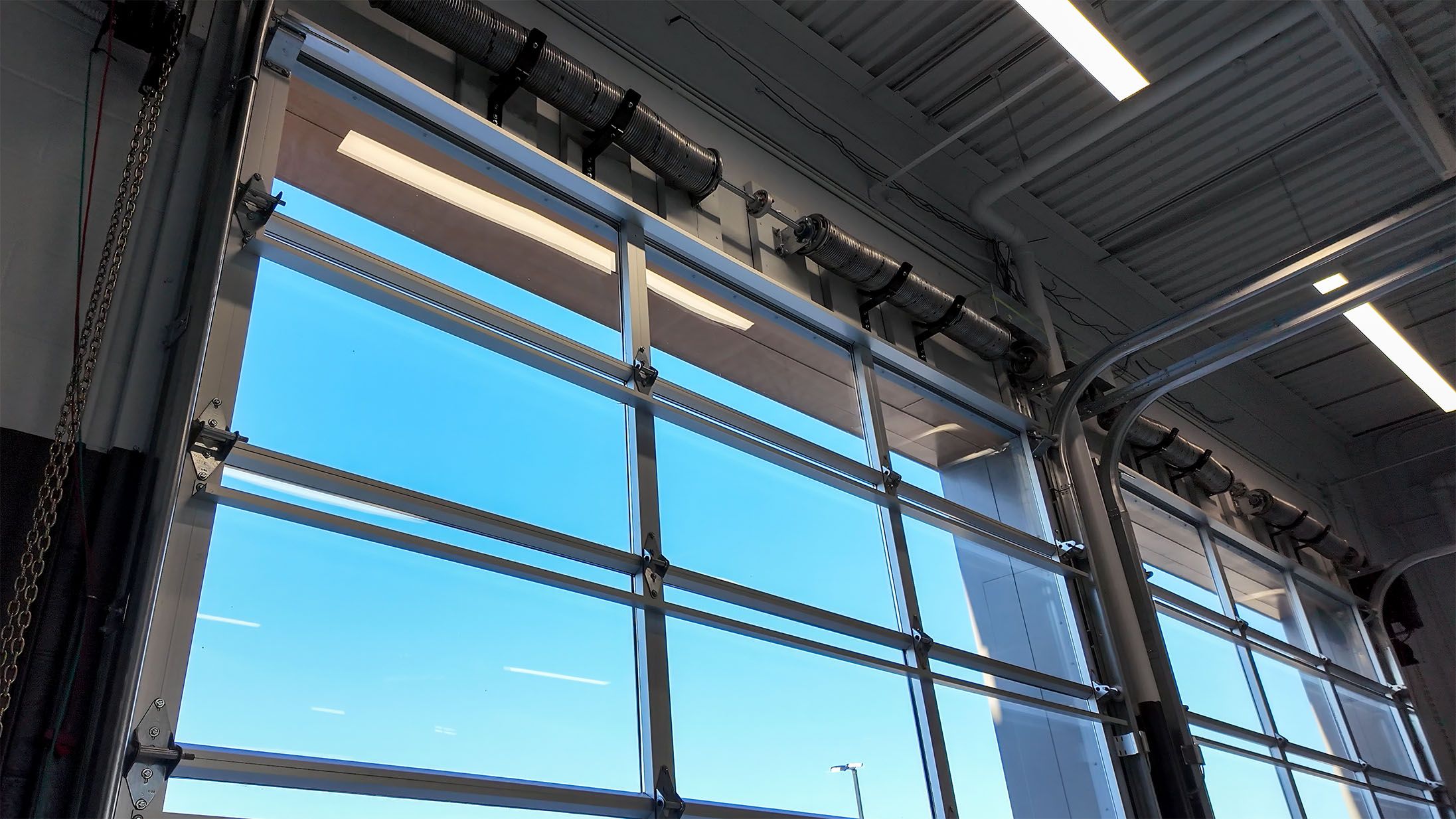 Interior view up at the head of a full-vision door showing torsion springs, torsion shaft, track and horizontal rails