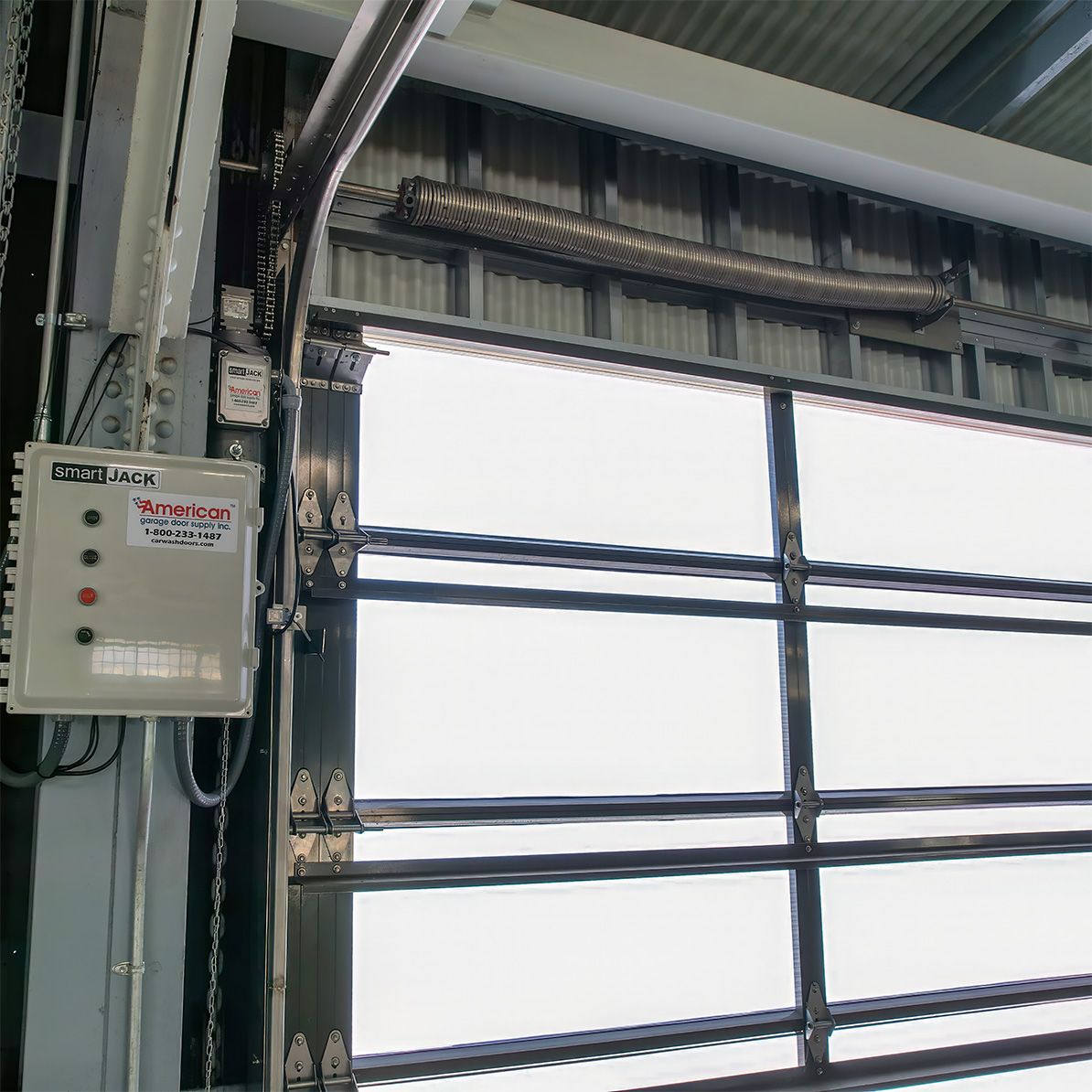SmartJack control box and chain-driven operator mounted beside a closed translucent door with the torsion spring above