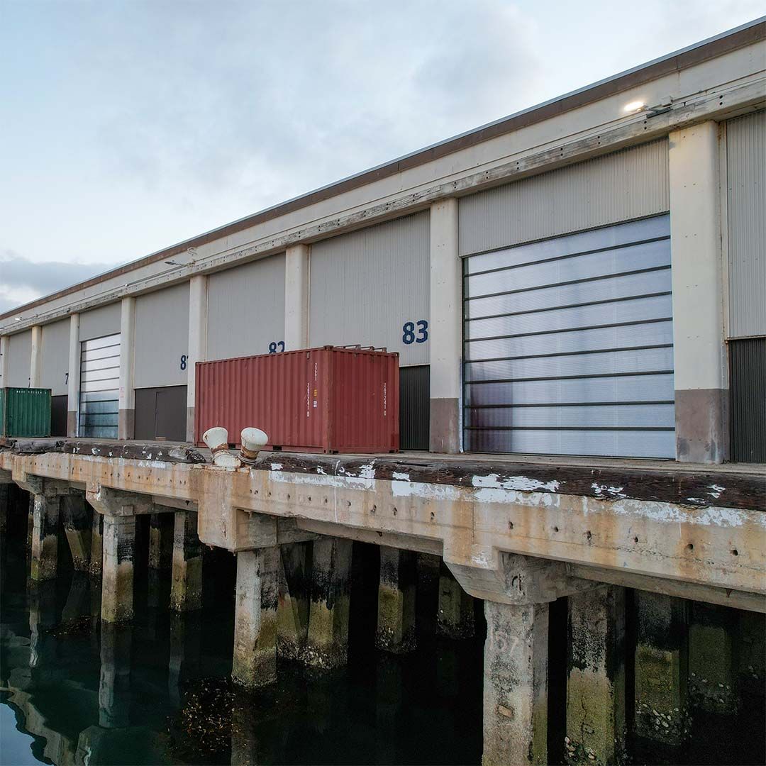 Closer exterior view of berth 83 with a closed translucent polycarbonate overhead door beside a shipping container